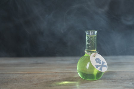 Flask of poison with warning sign on wooden table against dark background with smoke, space for textの写真素材