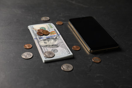 Smartphone, dollars and coins on black table, closeupの写真素材