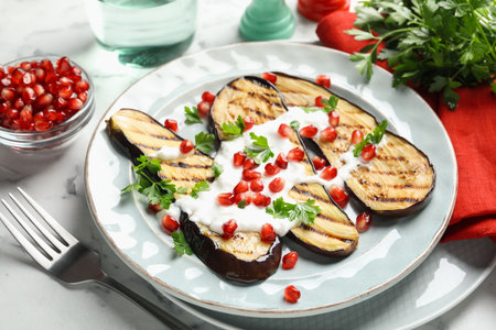 Slices of grilled eggplant with pomegranate seeds and yoghurt on white marble table, closeupの写真素材