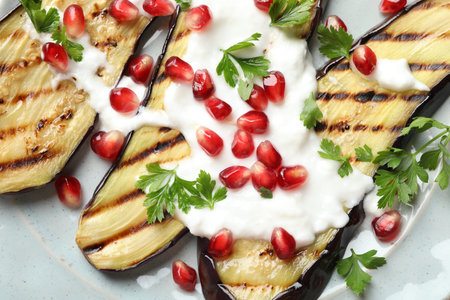 Slices of grilled eggplant with pomegranate seeds and yoghurt on tableの写真素材