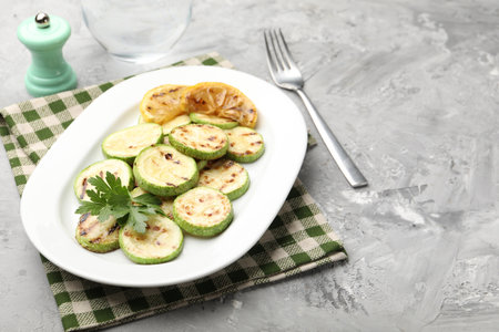 Delicious fried courgette slices with lemon and parsley served on grey table, closeup. Space for textの写真素材