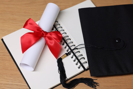 Graduation cap, diploma and notebook on wooden table, closeupの写真素材