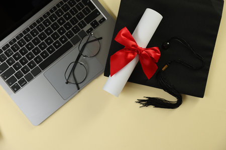 Graduation cap, laptop, diploma and glasses on beige background, flat lay. Space for textの写真素材
