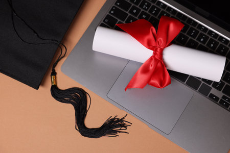 Graduation cap, laptop and diploma on beige table, flat layの写真素材