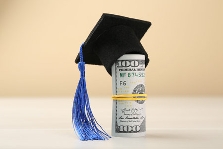 Scholarship. Graduate hat and dollar banknotes on white table against beige background, closeupの写真素材