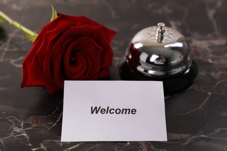 Card with word Welcome, desk bell and rose on black marble table, closeupの写真素材