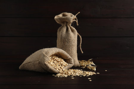 Oat flakes and sacks on dark wooden table against black backgroundの写真素材