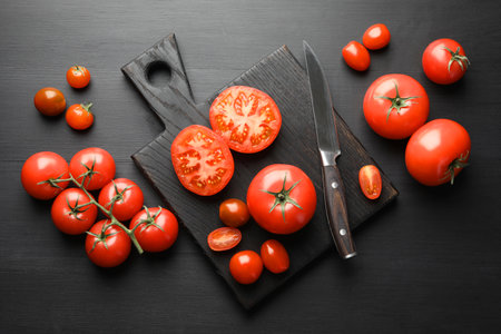 Whole and cut red tomatoes with knife on black table, flat layの写真素材