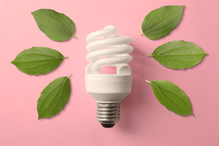Electricity and nature. Light bulb surrounded by green leaves on pink background, top viewの写真素材