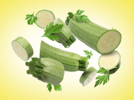 Pieces of fresh zucchinis and parsley falling on yellow gradient backgroundの写真素材