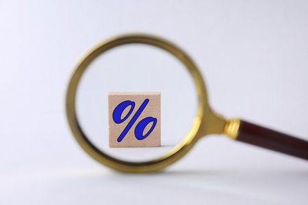 Percent sign on wooden cubes against light background, view through magnifying glassの写真素材