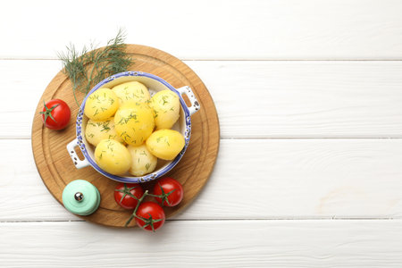 Tasty young boiled potatoes with dill in bowl, tomato and shaker on white wooden table, top view. Space for textの写真素材