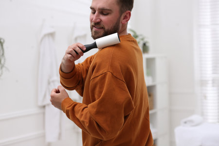 Young man cleaning clothes with lint roller at homeの写真素材