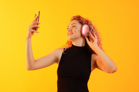 Happy woman with smartphone listening to music in headphones on yellow backgroundの写真素材