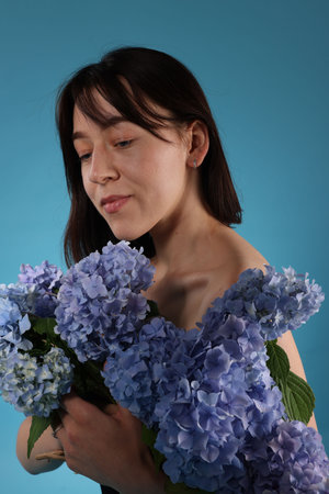 Beautiful young woman with hortensia flowers on blue background