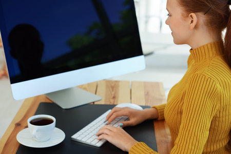 Teenage girl using computer at wooden desk indoors. Home workplace