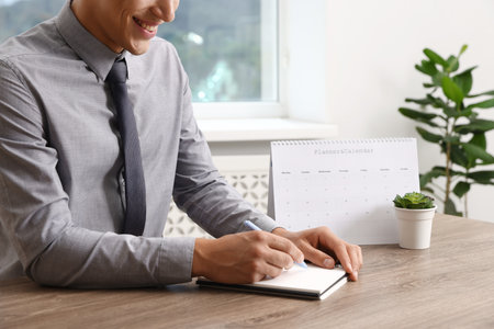 Man writing in business planner at wooden table in office, closeupの写真素材