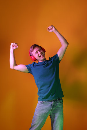 Smiling man wearing headphones listening to music in neon lights against orange backgroundの写真素材