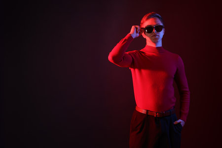 Handsome man wearing sunglasses in neon lights against dark background. Space for textの写真素材