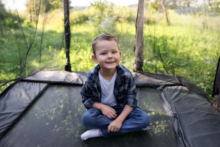Happy boy sitting on black trampoline outdoorsの写真素材