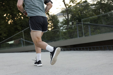 Athletic young man in sportswear running outdoors, closeup. Space for text