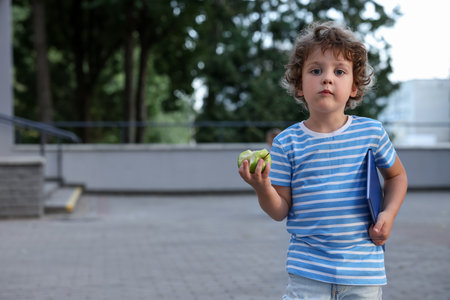 Cute little boy eating apple outdoors, space for text. School lunchの写真素材