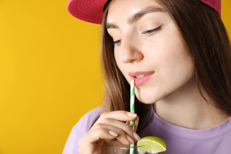 Woman drinking refreshing drink through straw on orange background, space for textの写真素材