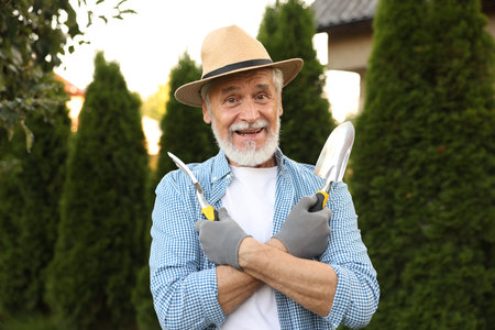 Portrait of smiling elderly man in hat with gardening tools outdoorsの写真素材