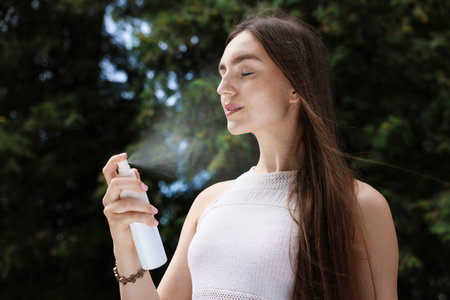 Smiling woman spraying thermal water from bottle outdoorsの写真素材