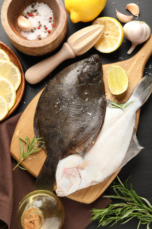 Fresh raw flounder fish, spices and juicer on black wooden table, flat lay. Seafoodの写真素材