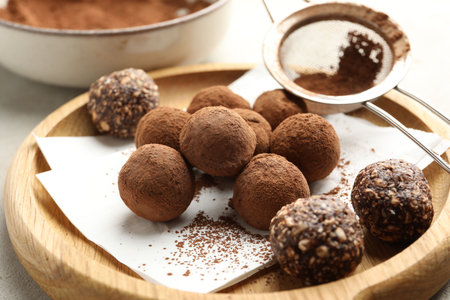 Tasty chocolate candies with cocoa powder and strainer on light table, closeup