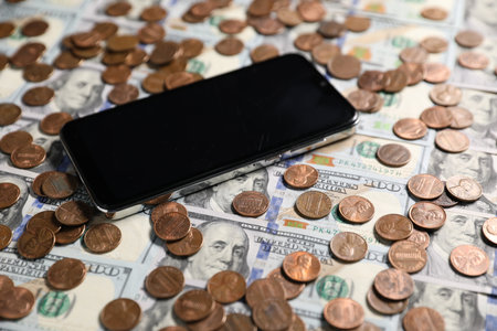 Smartphone and coins on dollar banknotes as background, closeupの写真素材