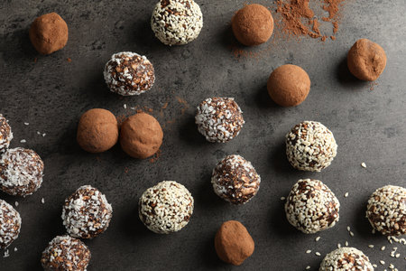 Tasty chocolate candies with cocoa powder, nuts, coconut flakes and sesame seeds on grey table, flat...