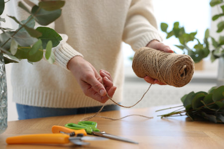 Florist with spool of thread making beautiful bouquet of eucalyptus branches at wooden table in...