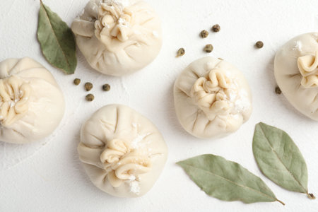 Uncooked khinkalis (dumplings) with peppercorns and bay leaves on white table, flat lay