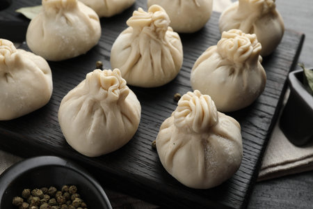 Uncooked khinkalis (dumplings) with peppercorns on black table, closeup