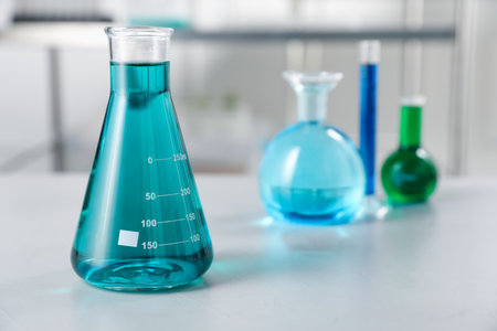 Different laboratory glassware with color liquids on light table indoors, selective focusの写真素材