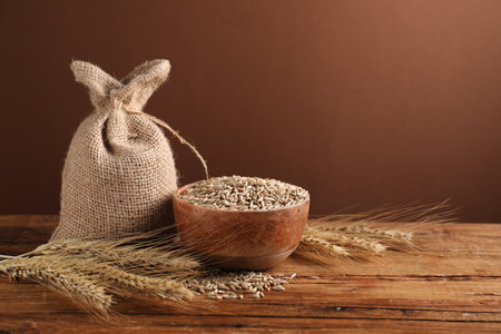 Rye grains in bowl, sack and spikes on wooden table against brown background, closeup. Space for textの写真素材