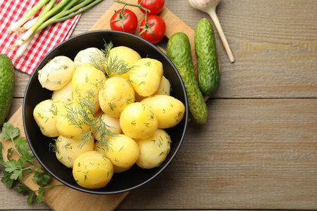 Tasty young boiled potatoes with dill in bowl and products on wooden table, flat lay. Space for textの写真素材