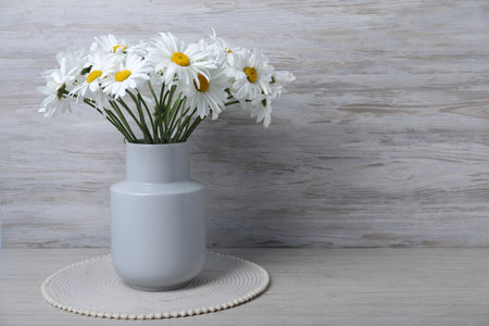 Beautiful chamomile flowers in vase on grey wooden table, closeup. Space for textの写真素材