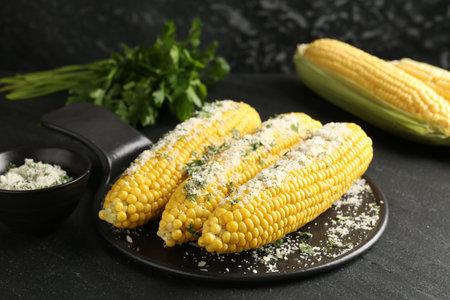 Tasty grilled corncobs with parsley and cheese on black table