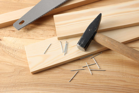 Metal nails, hammer, planks and saw on wooden table, above view
