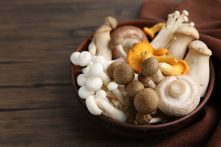 Different raw mushrooms in bowl on wooden table, closeup. Space for textの写真素材