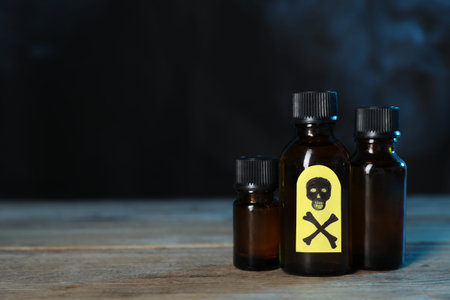Bottles of poisons with warning sign on wooden table against dark background with smoke, space for...