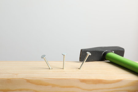 Metal nails in wooden plank and hammer on light grey background, closeupの写真素材