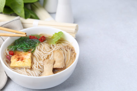 Tasty ramen with enoki and king oyster (eryngii) mushrooms on white table, closeup. Space for text