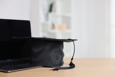 Graduation cap and laptop on wooden table indoors, closeup. Space for textの写真素材