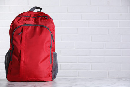 Red backpack on light marble table against white brick wall. Space for text