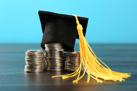 Scholarship. Graduate hat and coins on wooden table against light blue background, closeupの写真素材