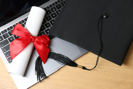 Graduation cap, laptop and diploma on wooden table, flat layの写真素材